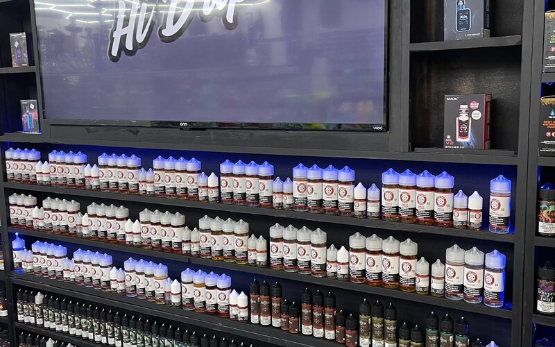 A wall of e-liquid bottles under a neon Hi Drip sign.